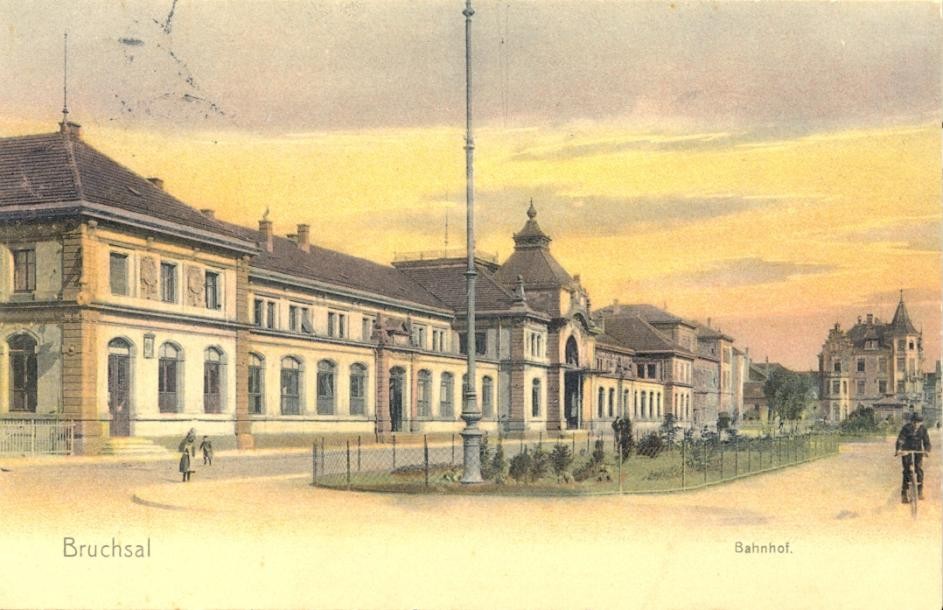 Postkarte des historischen Bahnhofsgebäude um 1900, nachkoloriert in Pastelltönen, rötlich schimmernder Himmel, Junge mit Fahrrad rechts, spielende Kinder links