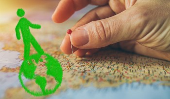 Eine Hand sticht eine Stecknadel in eine Weltkarte, davor symbolisiert ein grafisch dargestellte grüne Person und eine Weltkugel den nachhaltigen Zusammenhang