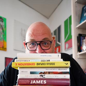 Ein Mann schaut hinter einem Bücherstapel hervor.
