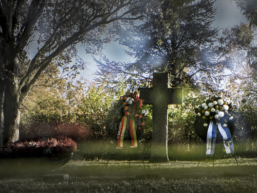 Zwei Blumenkränze und ein Grabstein in Form eines Kreuzes auf einem Friedhof