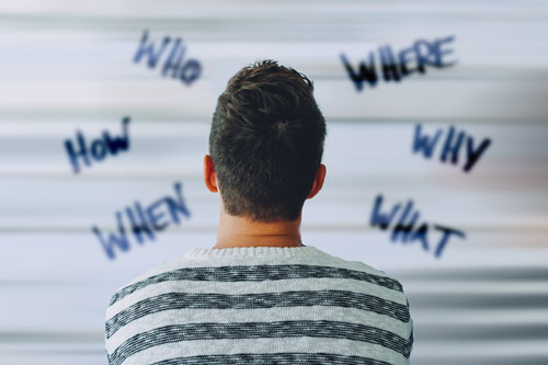 Soziale Betreuung Flüchtlinge/Asyl Person schaut auf eine Wand an der Who, How, When, Where, Why, What geschrieben steht
