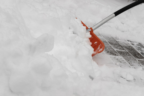 Rote Schneeschaufel, gepflasterter Boden und Schnee