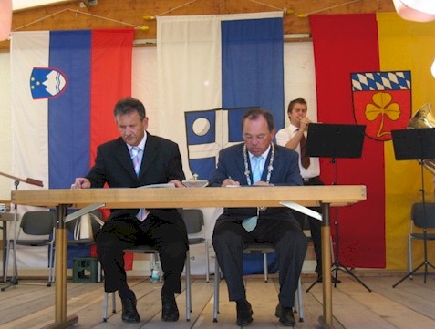 Oberbürgermeister a.D. Bernd Doll und Bürgermeister Anton Kampus unterzeichnen die Urkunden, im Hintergrund sind die Flaggen von Slowenien und Bruchsal zu erkennen