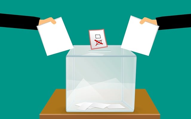 Zwei Hände werfen Wahlunterlagen in Wahlurnen 