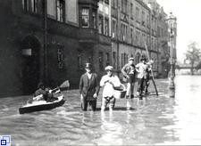 Vier Menschen stehen bis zu den Knie im Hochwasser, daneben ein Mensch im Kanu