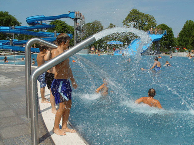 Kinder im Nichtschwimmerbecken mit Wasserkanonen, im Hintergrund blaue Rutsche
