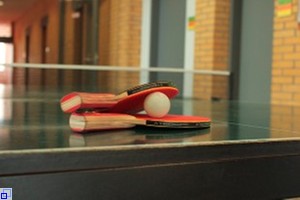 Zwei rote Tischtennisschläger und ein Ball liegen auf der grünen Tischtennisplatte